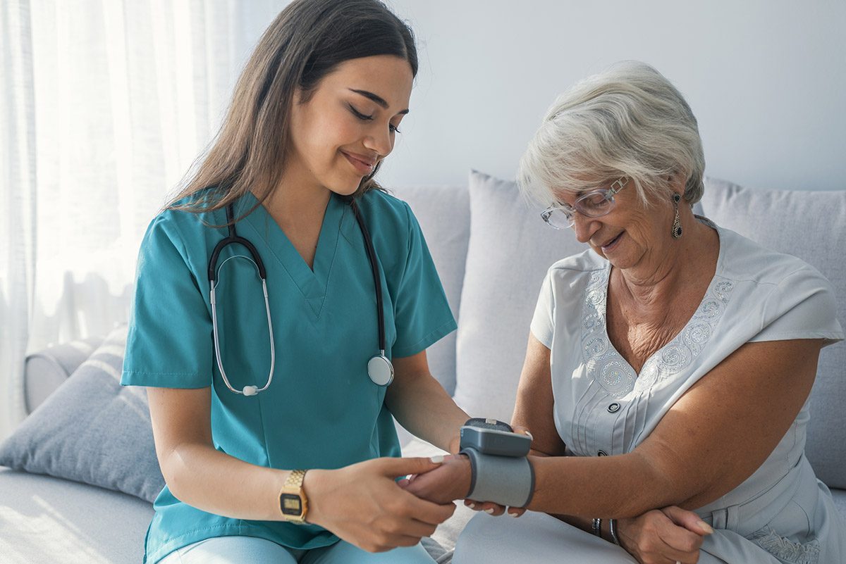 Caregiver measuring blood pressure of senior woman at home.